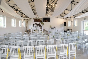 Ein geräumiger Saal mit Reihen aus weißen Stühlen, einer Bühne mit 'LOVE'-Hintergrund und einem Kronleuchter.