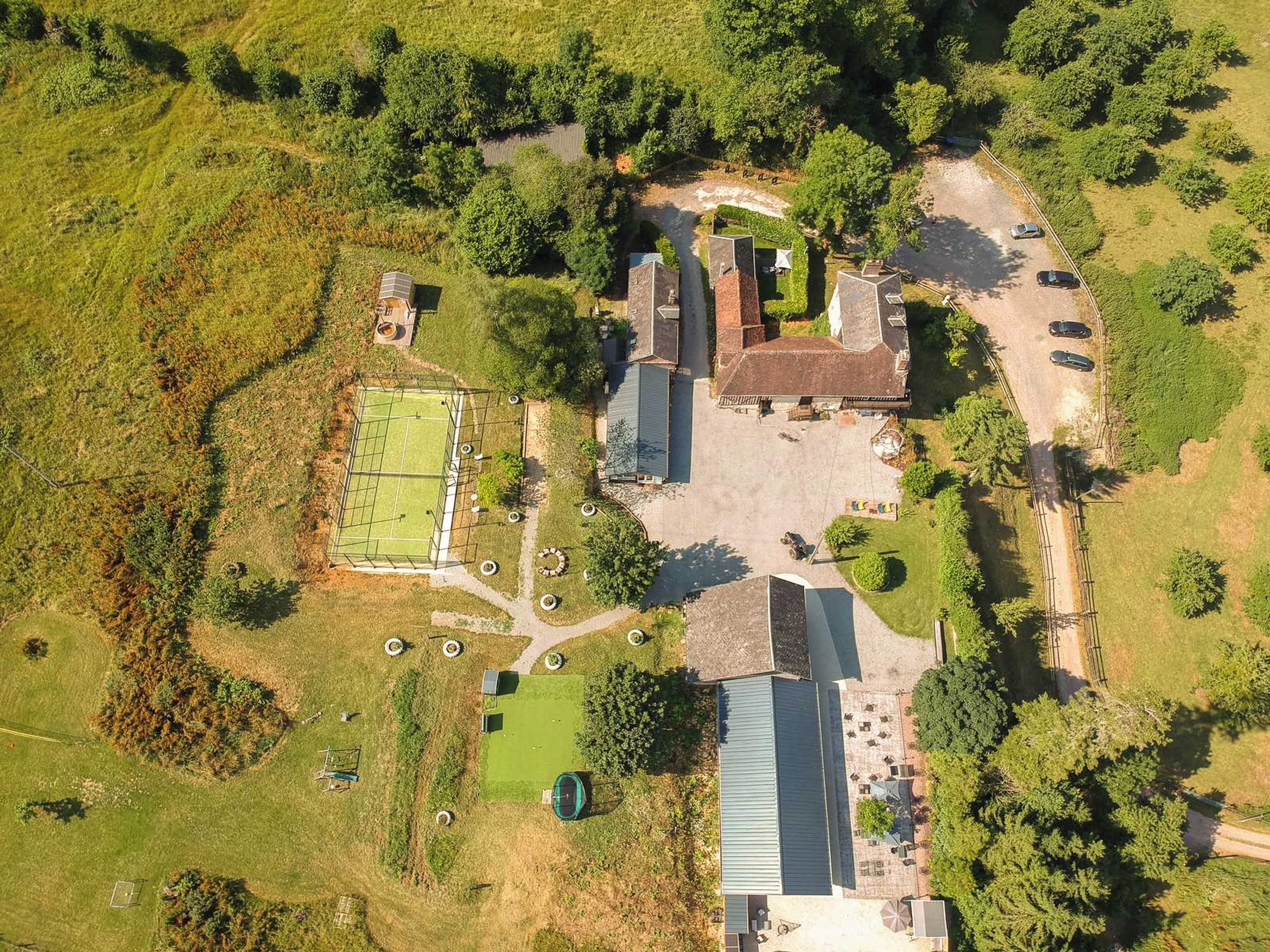 Vue aérienne d’une propriété comprenant un grand bâtiment central, plusieurs constructions plus petites et un terrain de sport.