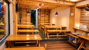A restaurant interior with wooden tables and benches, a staircase, and hanging pendant lights.