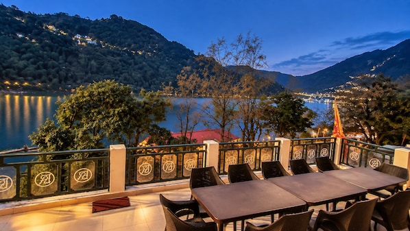 An outdoor dining area with a view of a lake and hills, featuring a table and chairs.