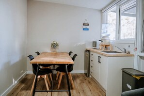 Eine kleine Küche mit Holztisch, schwarzen Stühlen, einer kompakten Spüle und einem Fenster mit Jalousien.