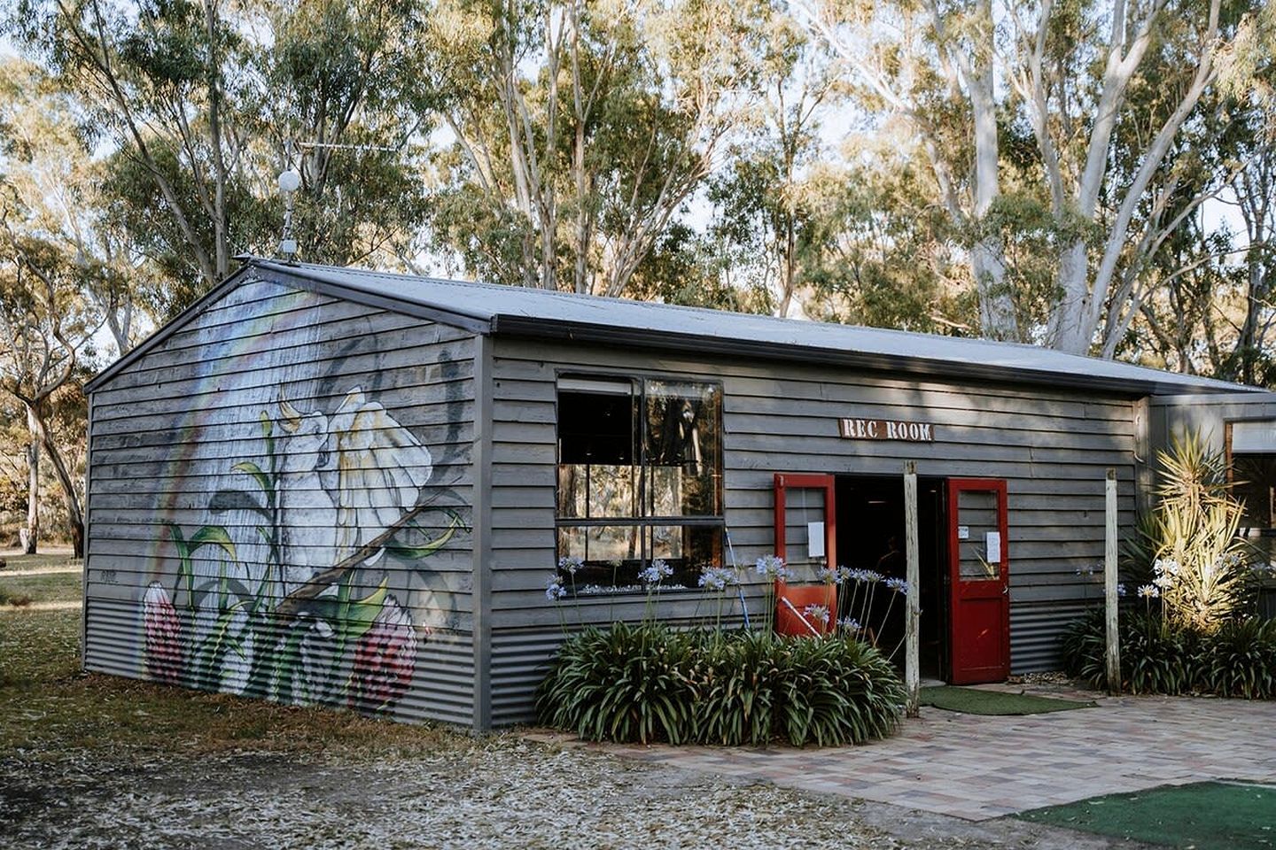 A small building with a mural on the side, a red door, and a sign that reads 'REC ROOM'.