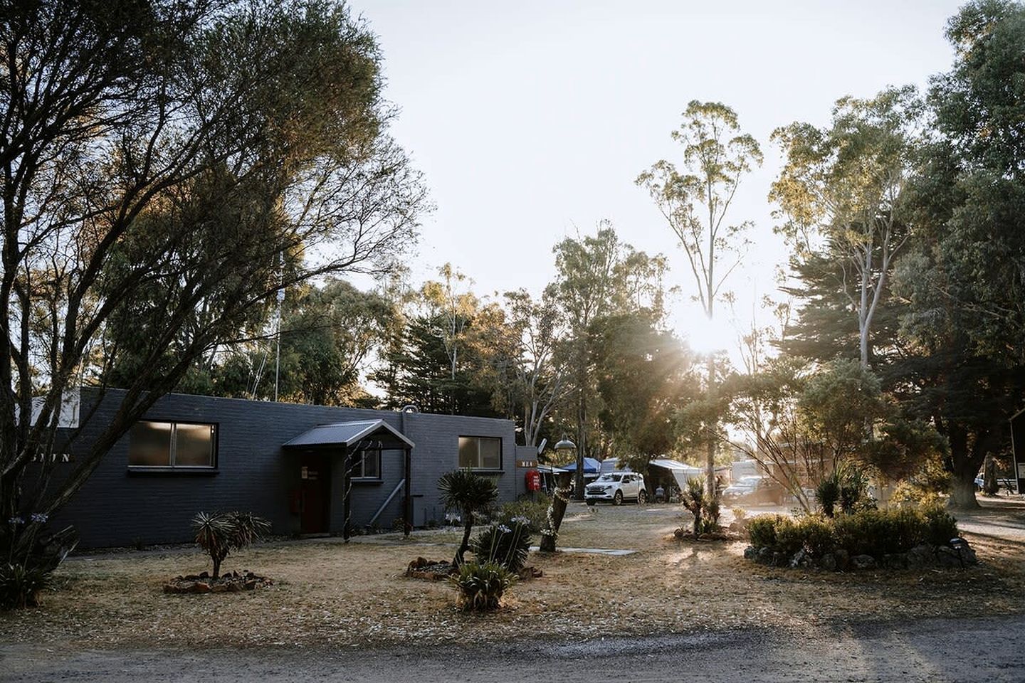 A modern building with a dark facade, surrounded by trees and a gravel driveway.
