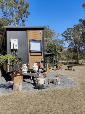 A compact mobile home with a small deck area, surrounded by potted plants and a gravel ground.