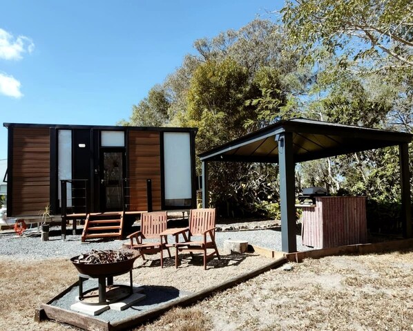 A modern outdoor seating area with a table and chairs, a fire pit, and a covered barbecue area.