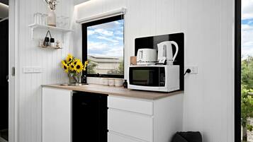 Een compacte keuken met een ingebouwde magnetron, een koffiezetapparaat en een raam met uitzicht op de omgeving.