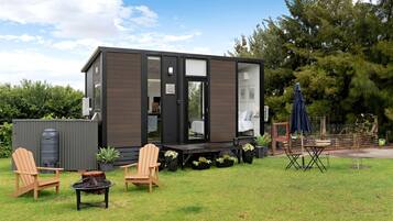 A compact, modern cabin with a deck, outdoor seating, and a water tank.