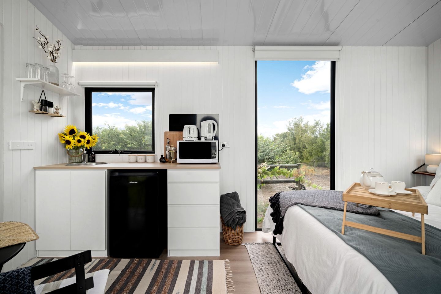 A compact room with a kitchenette, a bed, and a view of a garden.