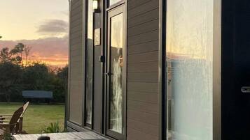 Een modern huis met een groot raam, een houten terras en een bankje.