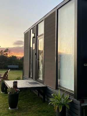 Una casa moderna con un ventanal grande, una terraza de madera y un banco.