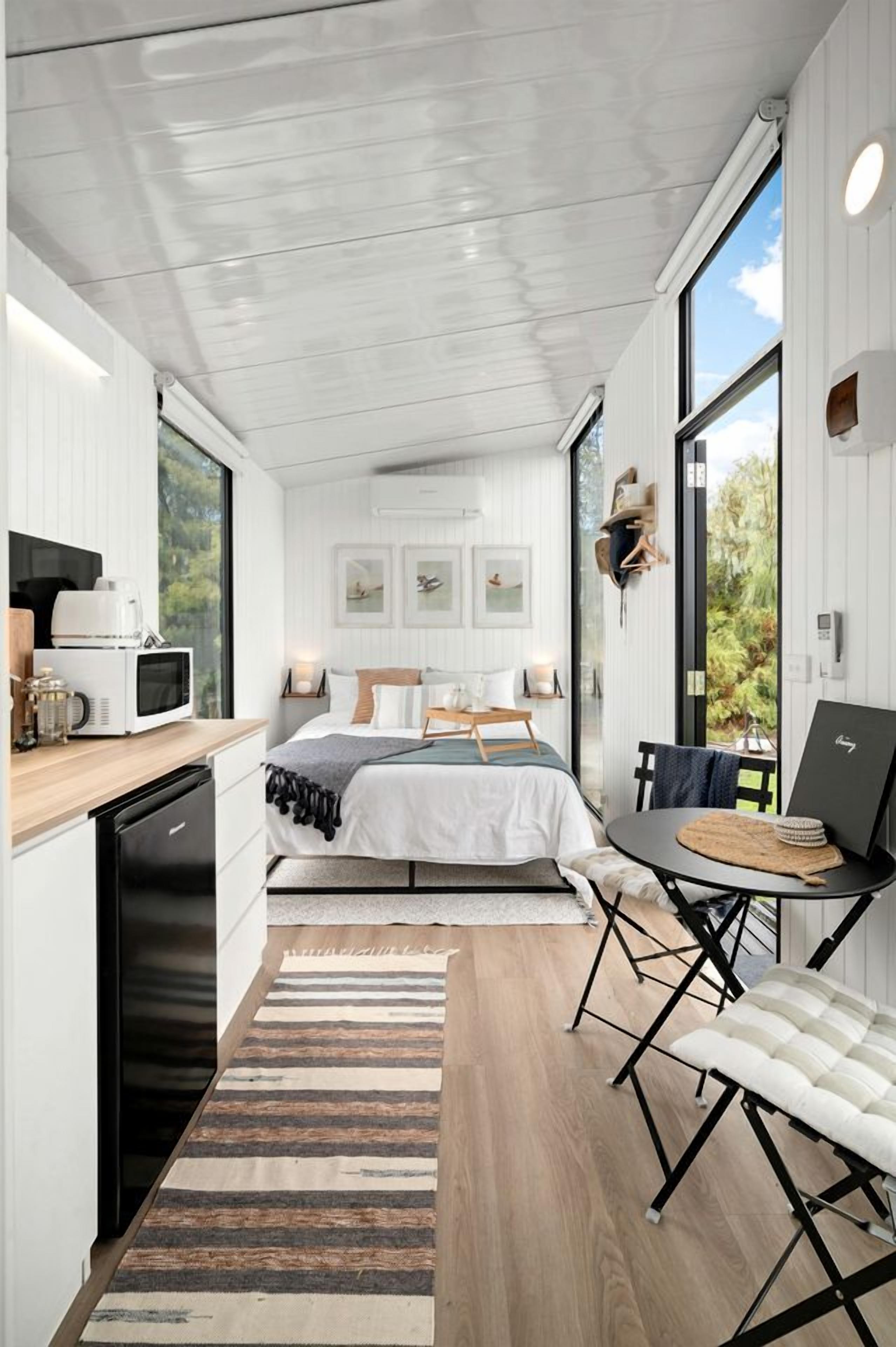 Een kleine slaapkamer met een bed, nachtkastje en een laptop op een bijzettafeltje.