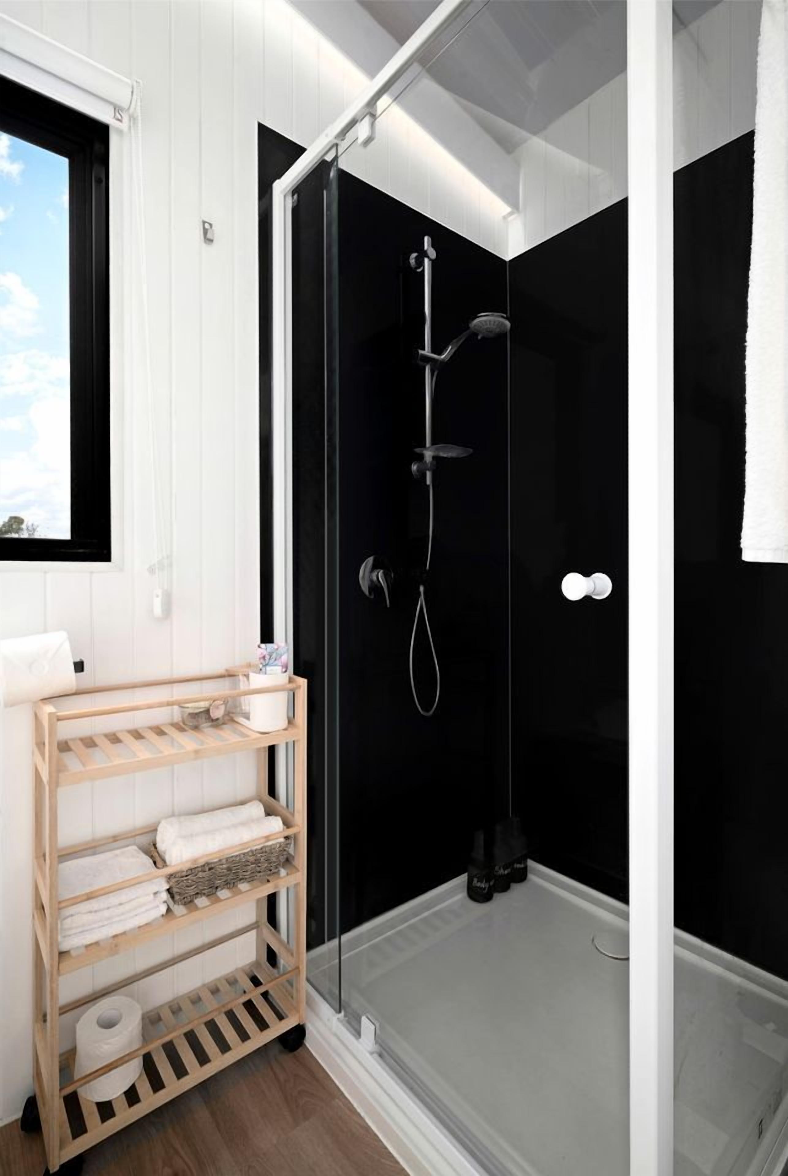 A modern bathroom with a glass-enclosed shower, a wooden towel rack, and a window with a view.
