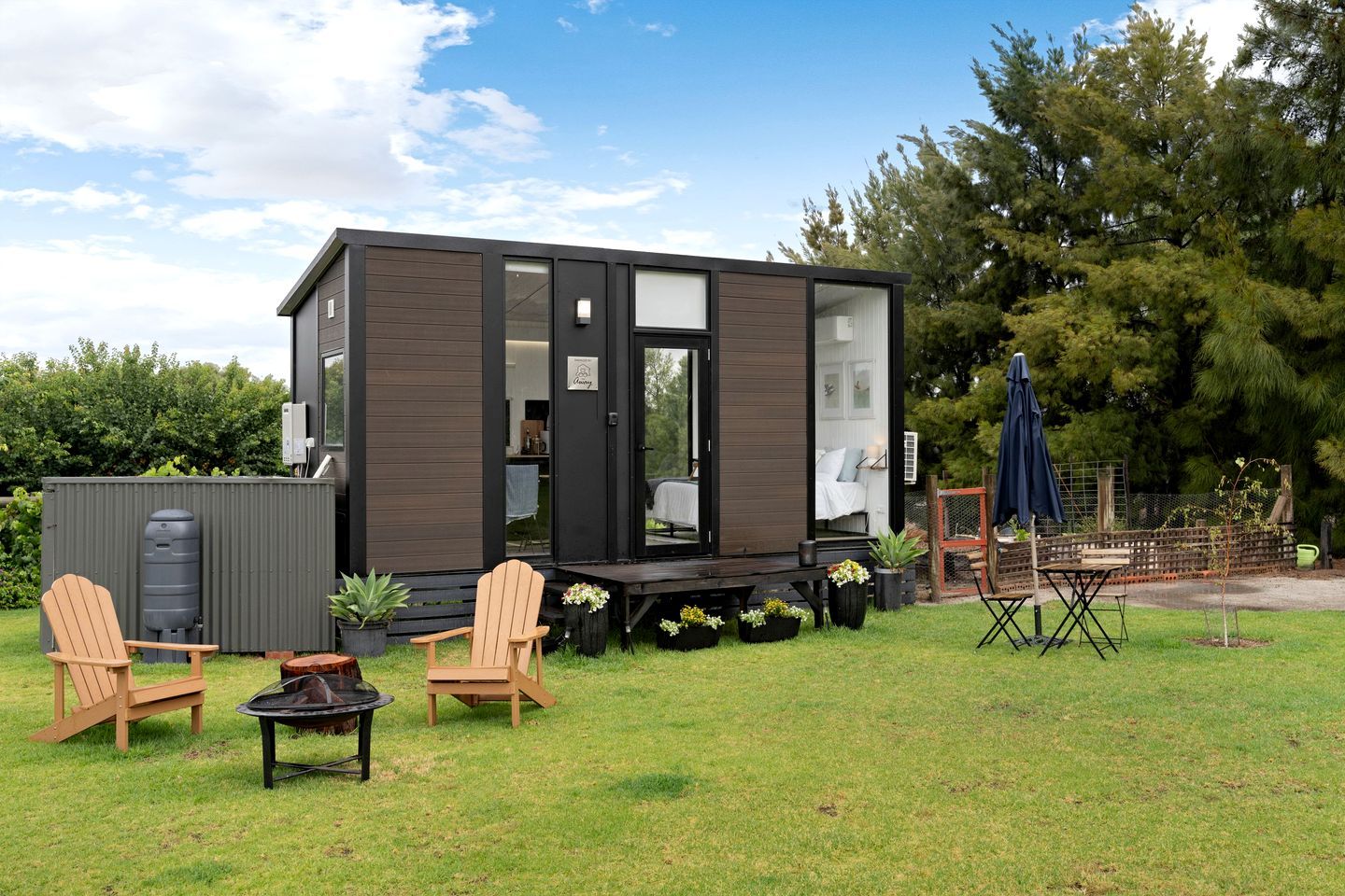 A compact, modern cabin with a deck, outdoor seating, and a water tank.