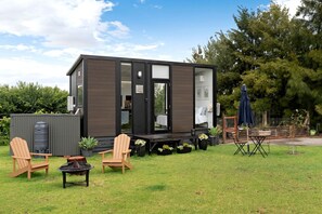 A compact, modern cabin with a deck, outdoor seating, and a water tank.