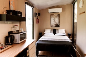 A compact hotel room with a bed, bedside tables, a microwave, a coffee maker, and a window.