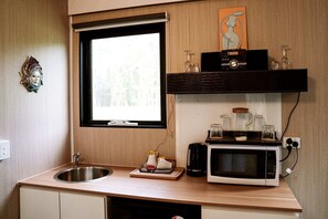 Una cucina compatta con una finestra, un forno a microonde, un lavandino e un piccolo ripiano con barattoli e una radio.