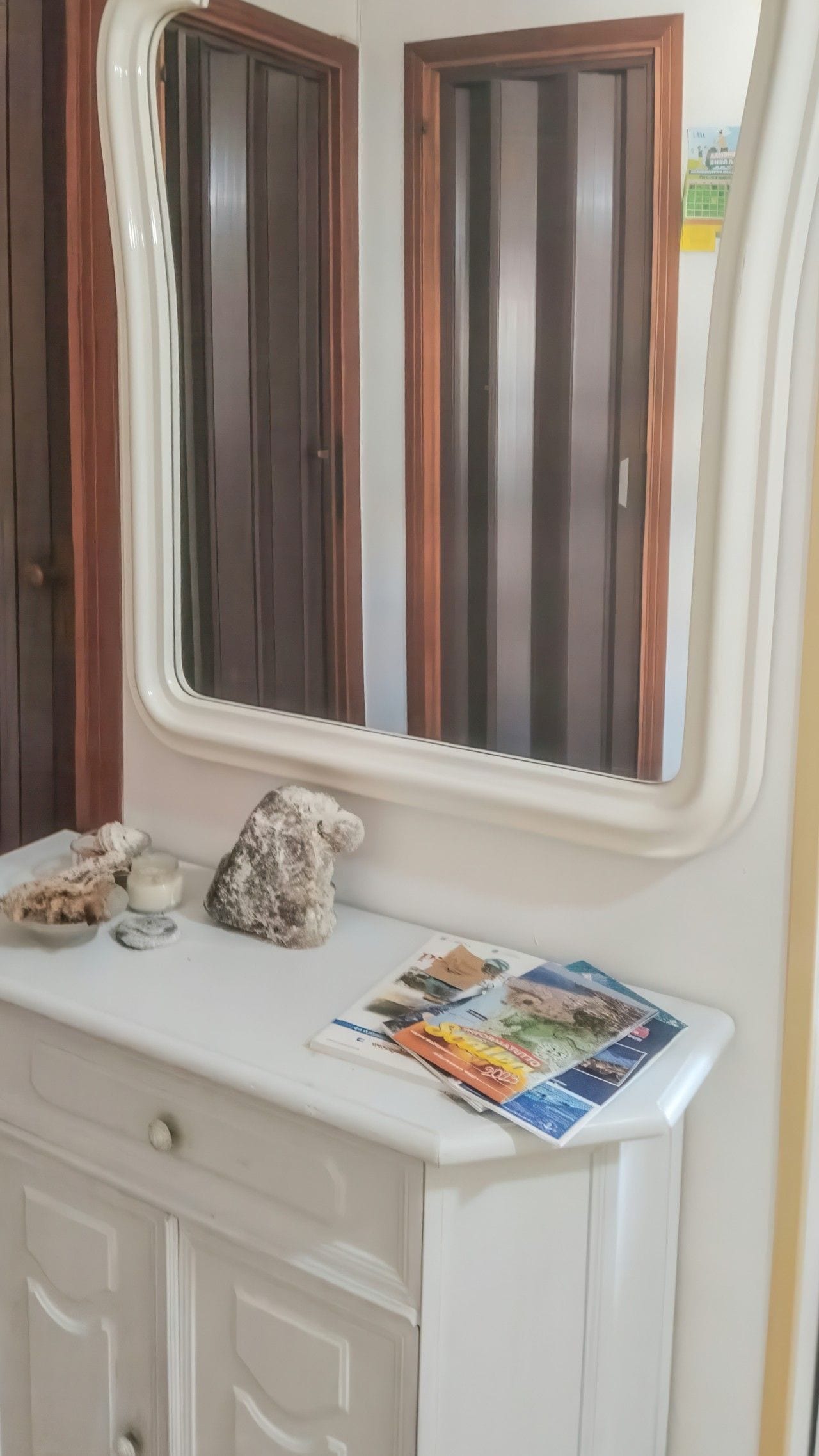 Een wastafelmeubel met spiegel, een klein plankje met toiletartikelen en een tijdschrift.