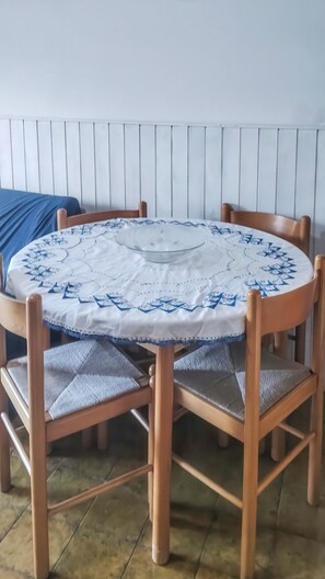 A round wooden table with a white tablecloth and blue patterns, surrounded by four wooden chairs with cushioned seats. - Eden Scalea—Cozy Apartment in a Condominium Complex in Scalea (Scalea)