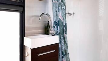 Un baño con ducha, un lavabo con espejo y un mueble de madera oscura.
