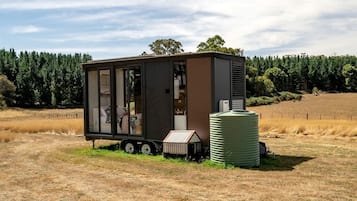 A small, modern mobile home with a large window, a water tank, and a trailer base.
