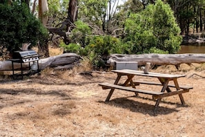A picnic table and a barbecue grill in a natural setting with trees and a log.