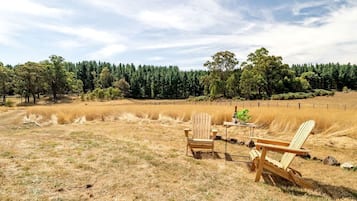 Entorno rural al aire libre con una silla de madera y una mesa, rodeado de hierba seca y árboles.