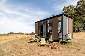 Uma casa móvel moderna e compacta com uma grande porta de vidro, área de estar externa e vista para a paisagem ao redor.