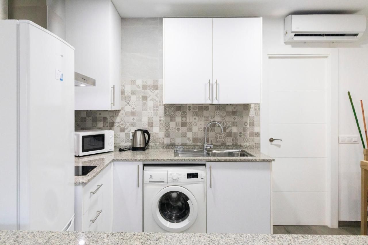 Cocina compacta con armarios blancos, microondas, lavadora y salpicadero de azulejos.