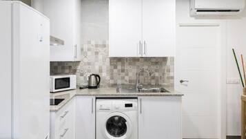 Cocina compacta con armarios blancos, microondas, lavadora y salpicadero de azulejos.