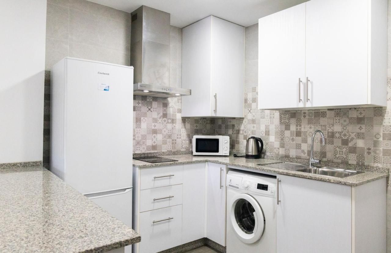 Una cocina compacta con refrigerador, microondas, hervidor y lavadora.