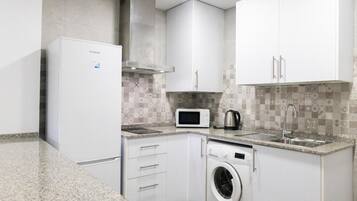 Una cocina compacta con refrigerador, microondas, hervidor y lavadora.