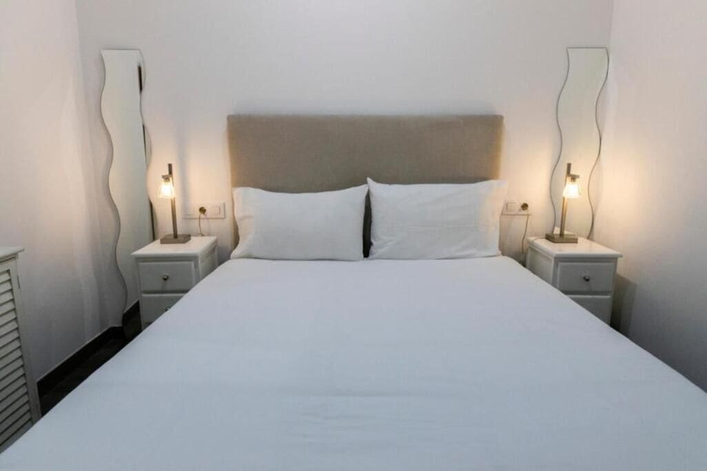 Una habitación de hotel con una cama grande, dos mesitas de noche y dos lámparas de pared.