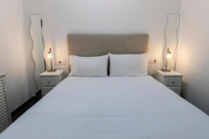 Una habitación de hotel con una cama grande, dos mesitas de noche y dos lámparas de pared.