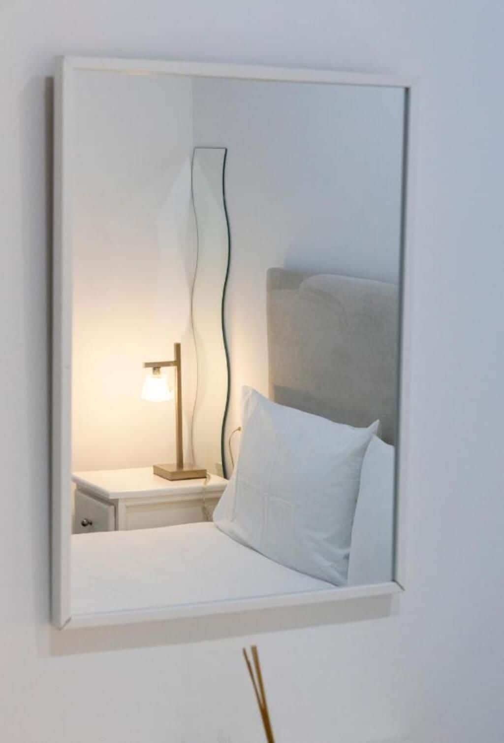 Un dormitorio con cama, mesita de noche, lámpara y espejo.