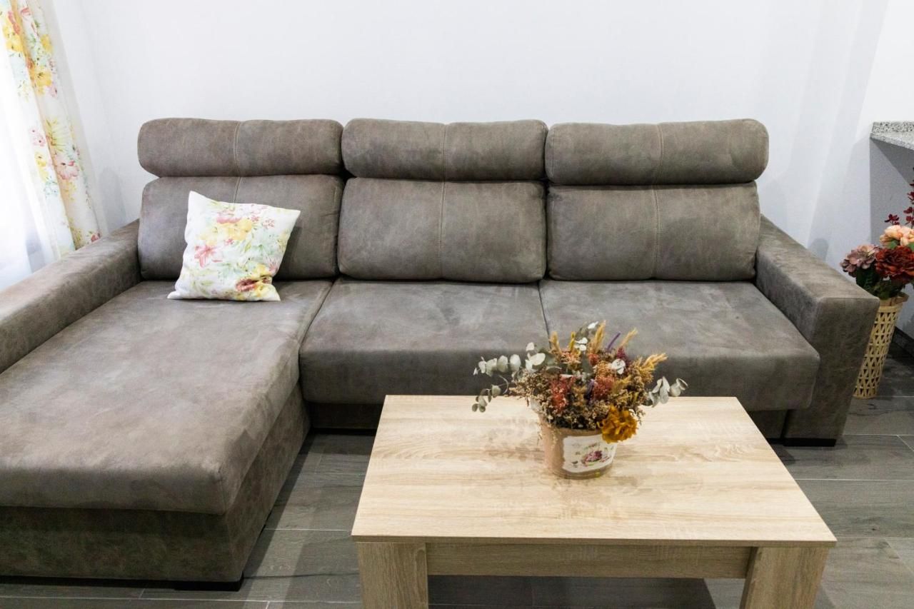 Un sofá gris con un cojín estampado y una mesa de centro de madera con un arreglo floral.