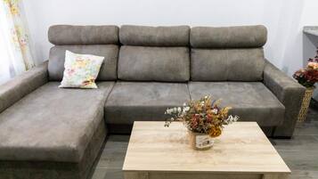 Un sofá gris con un cojín estampado y una mesa de centro de madera con un arreglo floral.