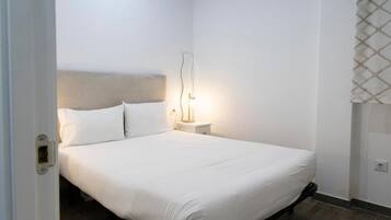 Una cama bien hecha en una habitación de hotel, con una mesita de noche y una lámpara.