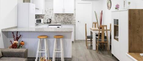 Una cocina moderna con armarios blancos, una isla central con taburetes y un comedor con sillas de madera.
