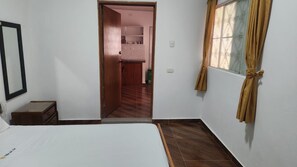 A bedroom with a bed, a wooden door leading to a kitchen, and a window with curtains. - Your ideal getaway: an apartment 5 m from Honda (Puerto Bogotá, Guaduas)