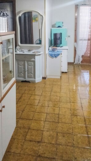 A kitchen with a tiled floor, a white cabinet with glass doors, a sink, and a countertop with various items. - Eden Scalea (Scalea)