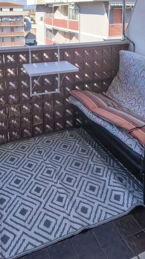 A balcony with a patterned rug, a sofa with striped cushions, and a small white table. - Eden Scalea (Scalea)