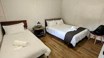 Une chambre d’hôtel avec deux lits, une table de chevet avec une lampe, une chaise et une petite plante.