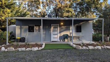 A single-story building with a covered porch, a door, and a small outdoor seating area with a bench.