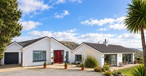Ein zweistöckiges Haus mit roter Tür, einer Garage und einer Terrasse mit Gartenmöbeln.