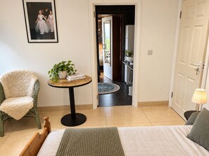 A bedroom with a bed, a chair, a small table with a plant, and a door leading to a bathroom. - Atlantic Golf Retreat near Waterville (Cahersiveen)