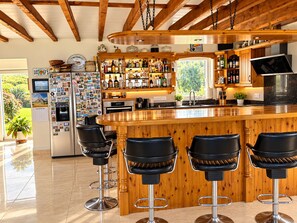 A bar area with a wooden bar counter, four black bar stools, and a refrigerator with magnets. - Atlantic Golf Retreat near Waterville (Cahersiveen)
