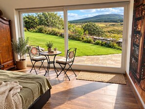 A room with a bed, a dining table with chairs, a view of a garden, and a bookshelf. - Atlantic Golf Retreat near Waterville (Cahersiveen)