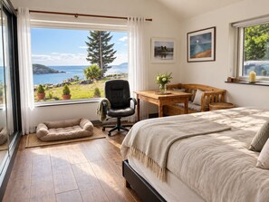 Ein Schlafzimmer mit einem großen Bett, einem Schreibtisch, einem Sessel, einer kleinen Couch und Meerblick.