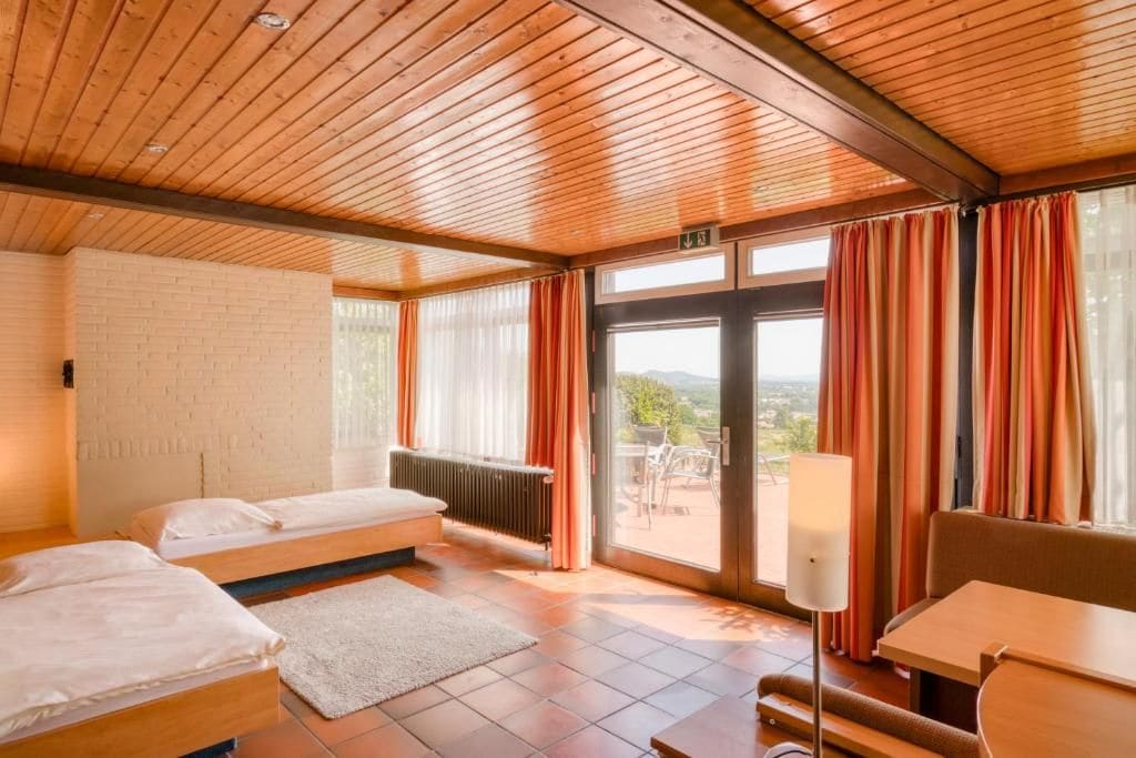 Ein Zimmer mit zwei Betten, einem Heizkörper, einem Tisch und Blick durch eine Glastür.
