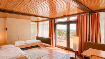 Ein Zimmer mit zwei Betten, einem Heizkörper, einem Tisch und Blick durch eine Glastür.